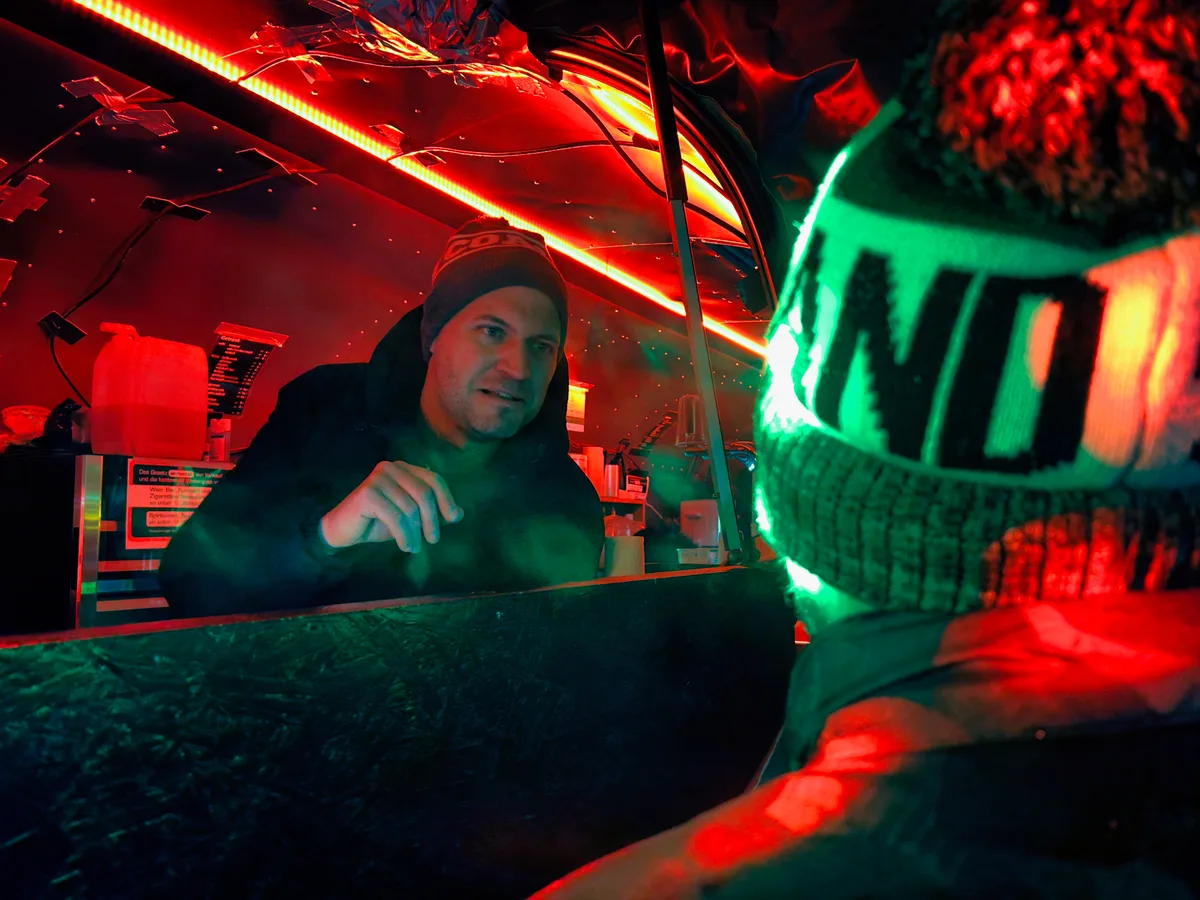 Man sieht einen Mann, der über die Theke eines Foodtrucks mit einem anderen spricht.